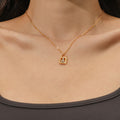 A close-up of a model's neck and chest wearing a delicate gold chain necklace with a small padlock-shaped pendant featuring a clear gemstone.