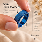 A close-up of a person's fingers holding a blue metallic ring with a textured outer band, set against a soft beige background with promotional text and icons about spinning the ring.