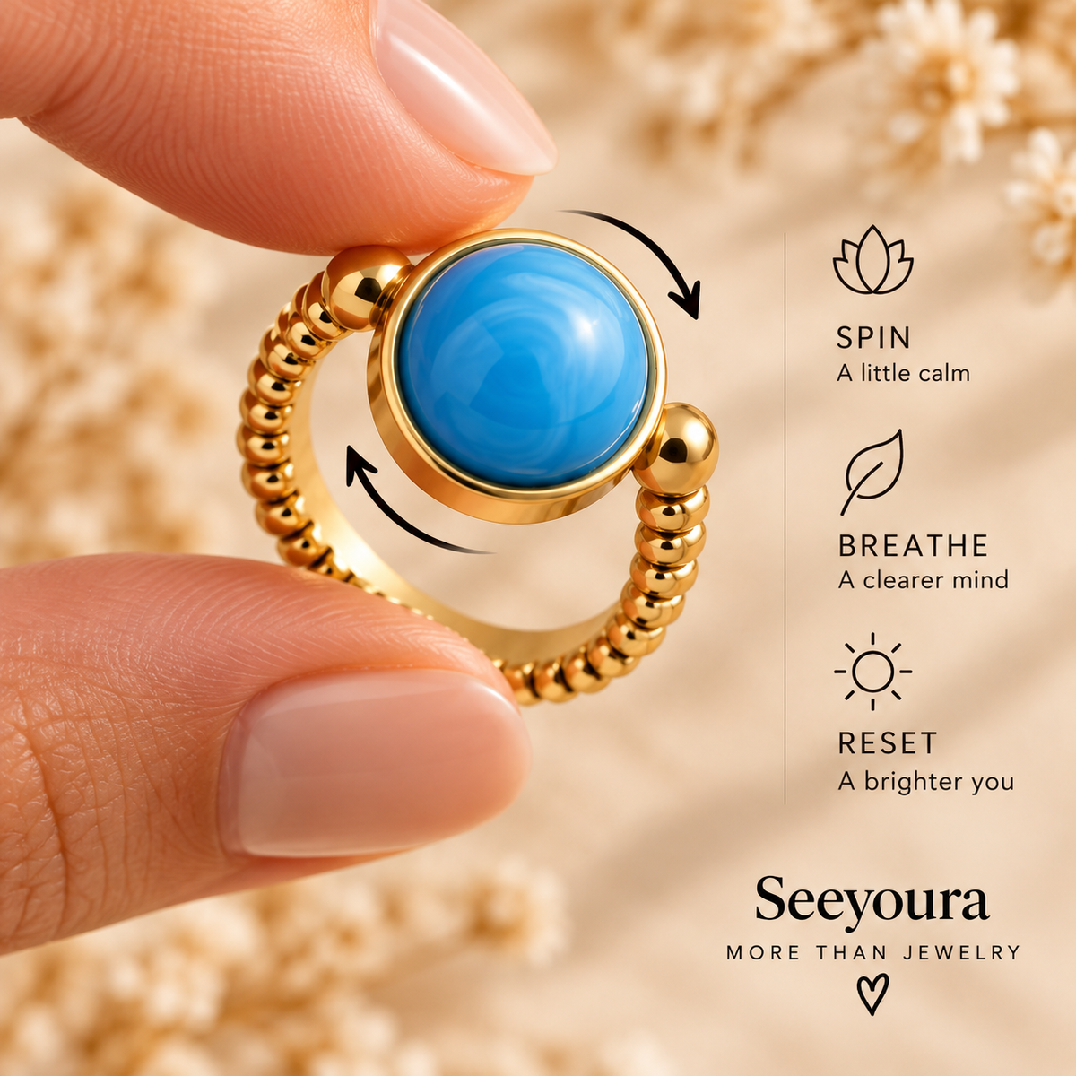 A close-up of a hand holding a gold ring with a round blue stone. The ring has a textured beaded band and arrows showing it can be spun.