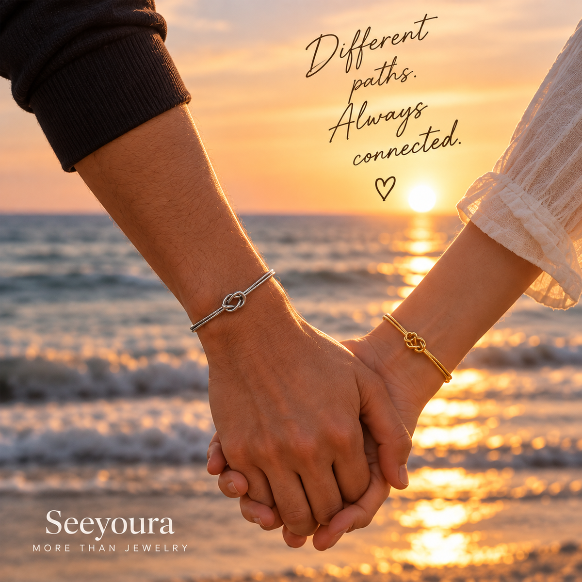 Two people holding hands on a beach at sunset, each wearing a delicate bracelet. One bracelet is silver with an infinity-style knot, and the other is gold with a matching knot.