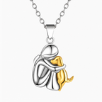 A two-tone silver and gold pendant necklace featuring a mother hugging her puppy. The pendant is made of polished silver and gold metal, suspended from a silver link chain against a clean white background.